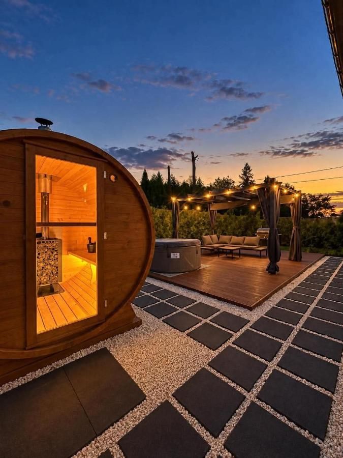 Sauna-beczka o zachodzie słońca, w tle taras z pergolą i lampkami